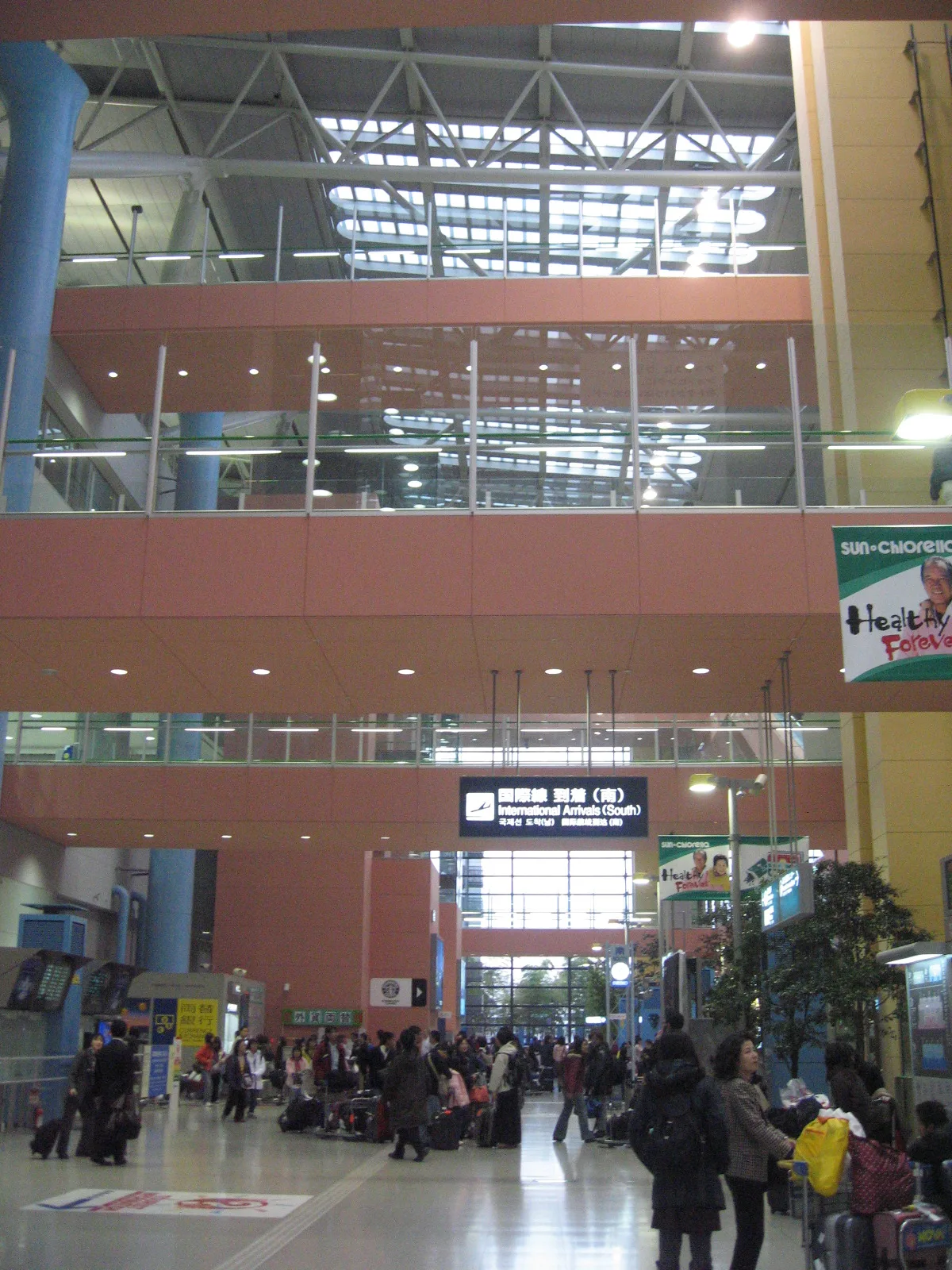 Passengers with luggage in the arrival hall of Kansai International Airport, below an "International Arrivals (South)" sign.