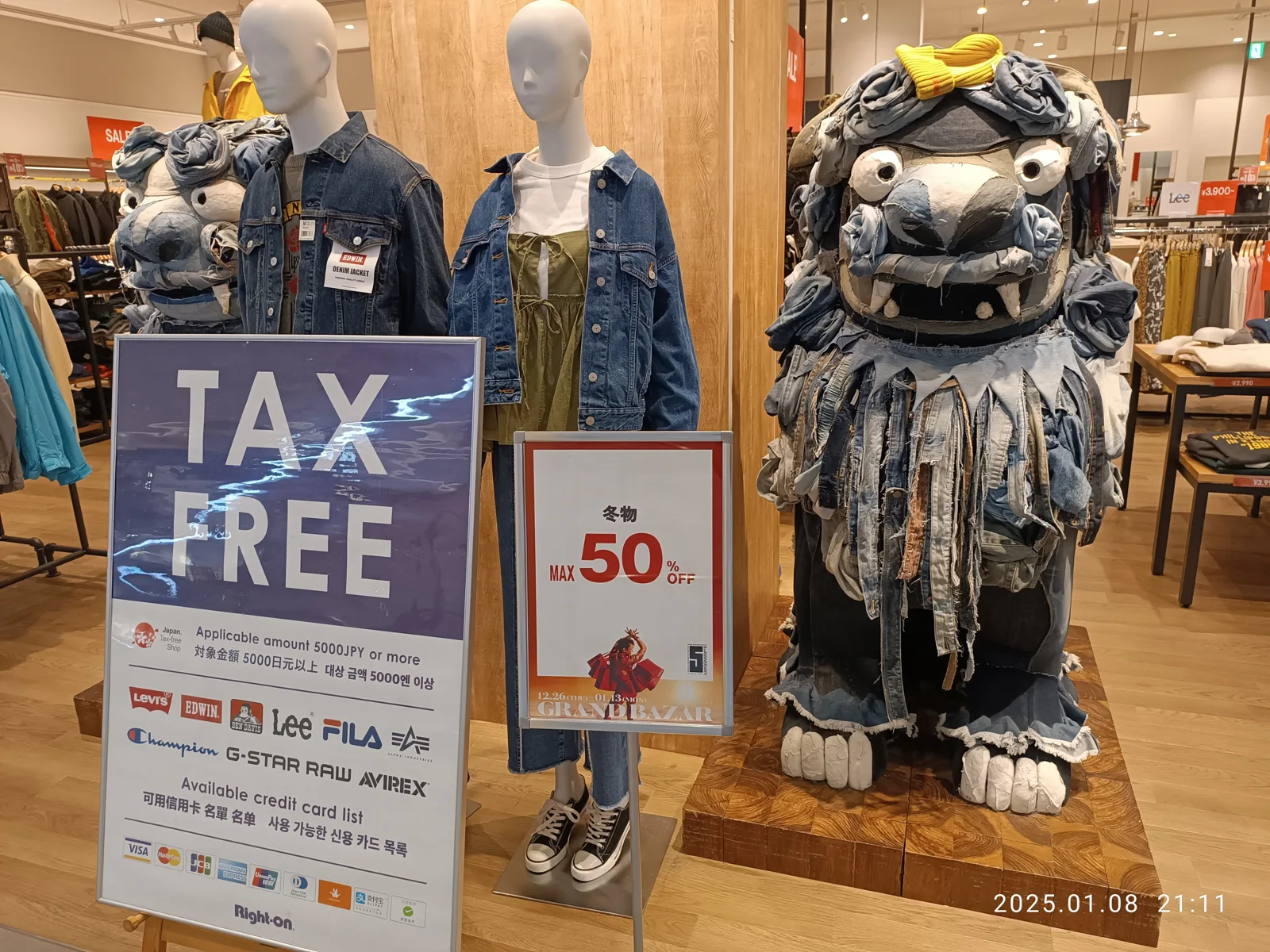 A tax-free sign beside denim-dressed mannequins and a shisa lion-dog statue in a clothing shop at PARCO City Mall, Okinawa (photo from January 2025, before the 2026 change).