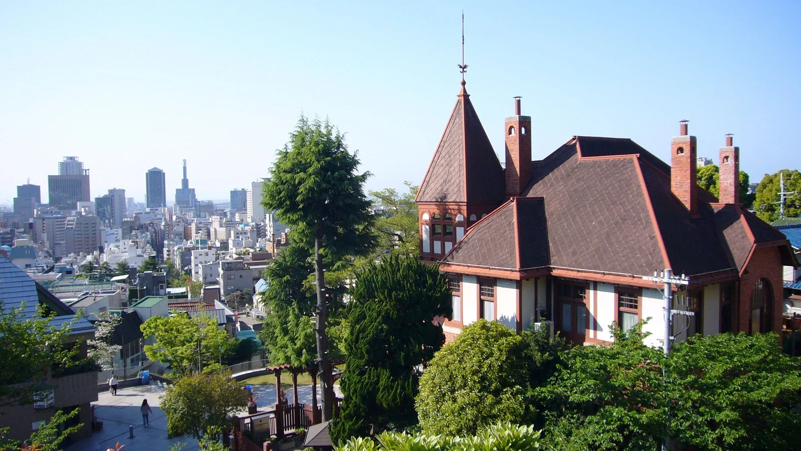 The Weathercock House in Kobe's Kitano-cho, with its red brick tower and weathervane spire, seen against the city skyline on a clear day.