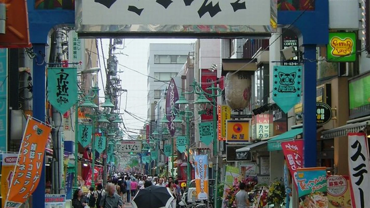 The entrance archway to Togoshi Ginza shopping street in Shinagawa, Tokyo, with green shop banners, string lanterns and pedestrians filling the street beyond the gate.